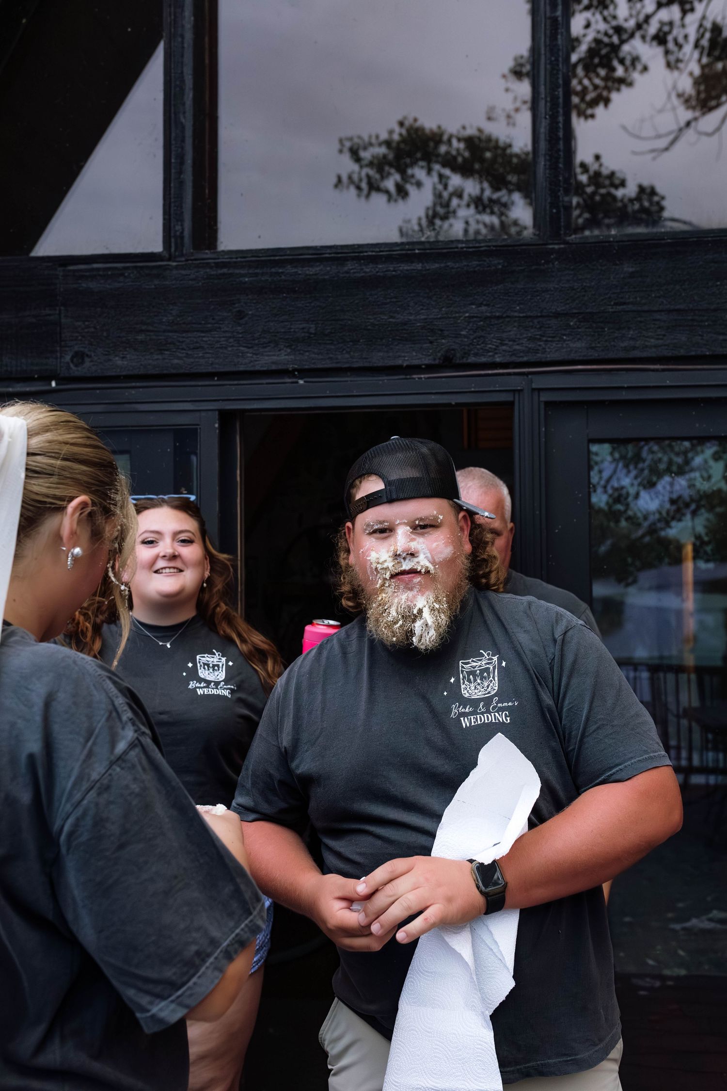 Man with wedding cake smeared on his face smiling at an outdoor wedding celebration.