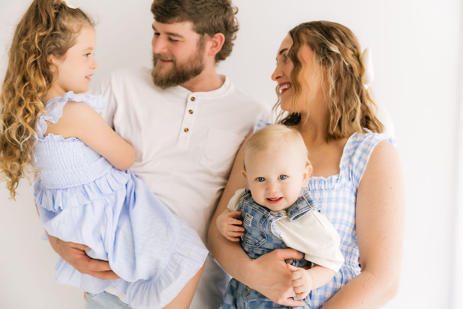 Happy family of four with two young children smiling together against bright white studio background.
