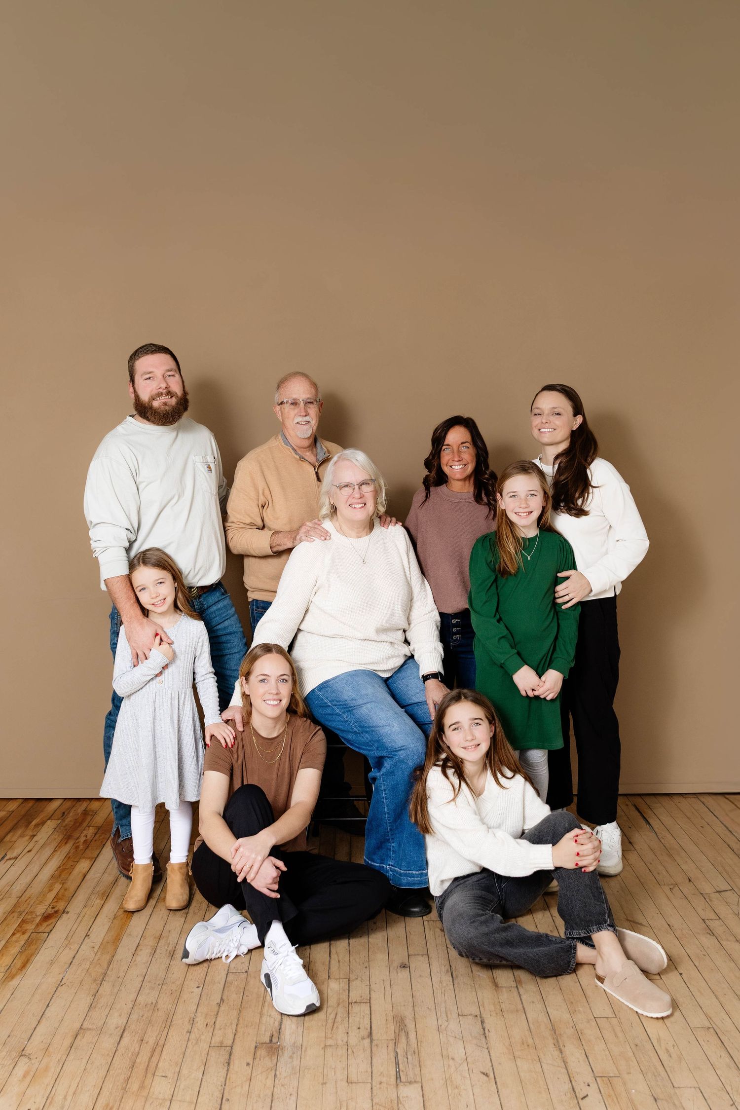 Multi-generational family portrait posing together against a warm tan studio background.