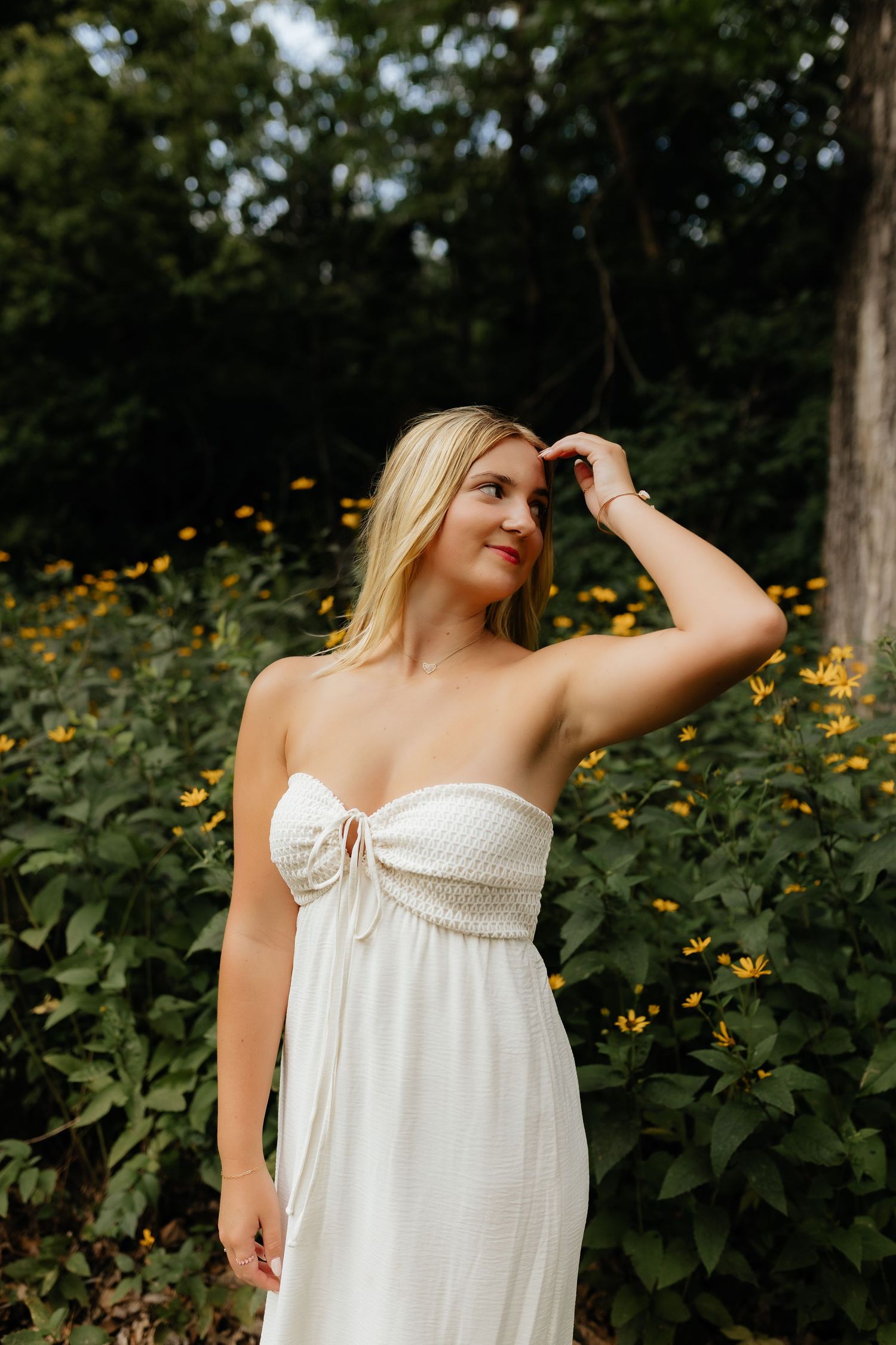 Blonde woman in white strapless dress posing among vibrant yellow wildflowers in a garden.