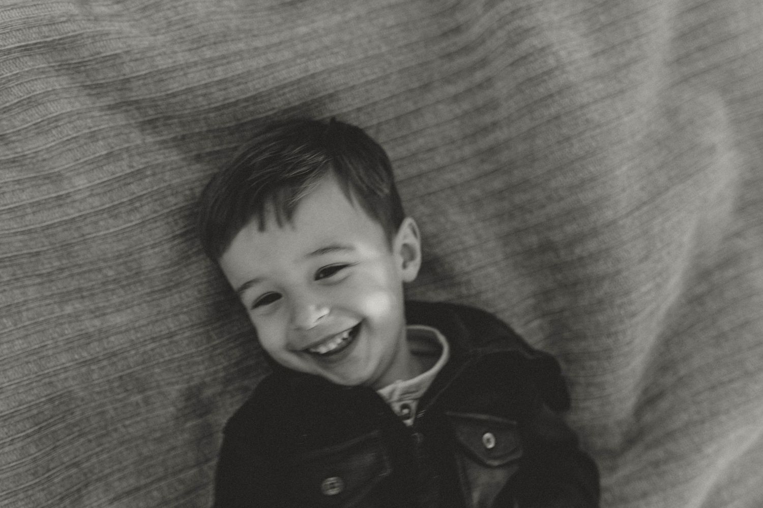 Happy toddler boy smiling while lying down in black and white portrait photo.