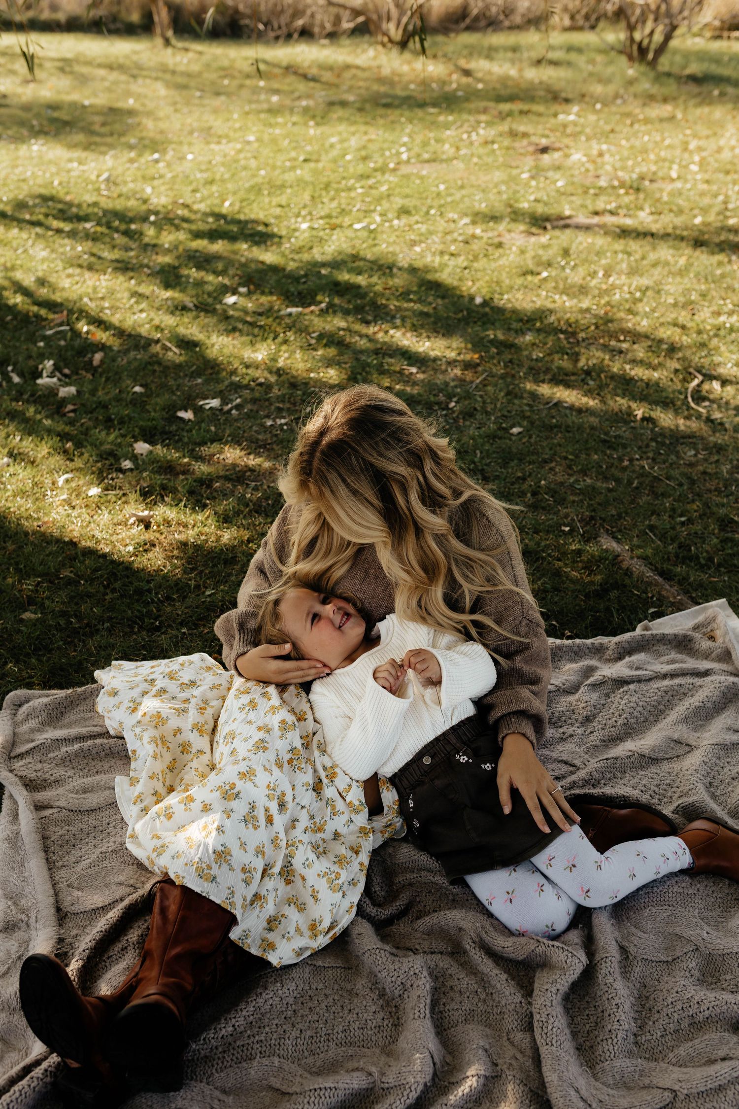 Mother tenderly gazing at her baby on a blanket outdoors in a sunny green park setting.