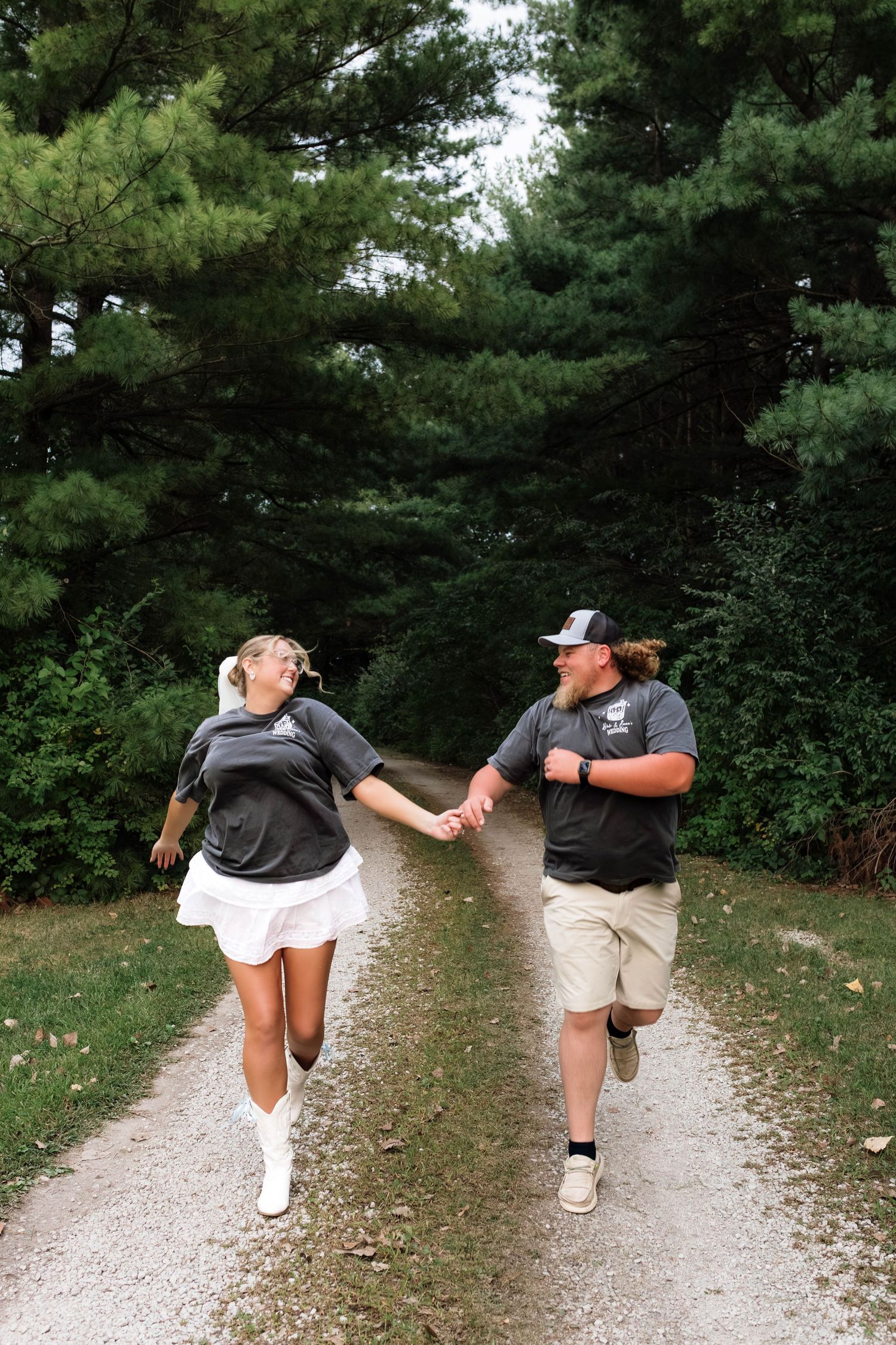 Bride and groom running hand in hand down a scenic tree-lined gravel path.