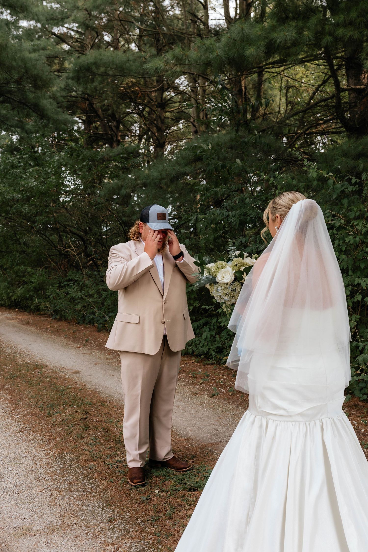 Emotional groom covering his face with a cap during first look as bride approaches in a white gown.
