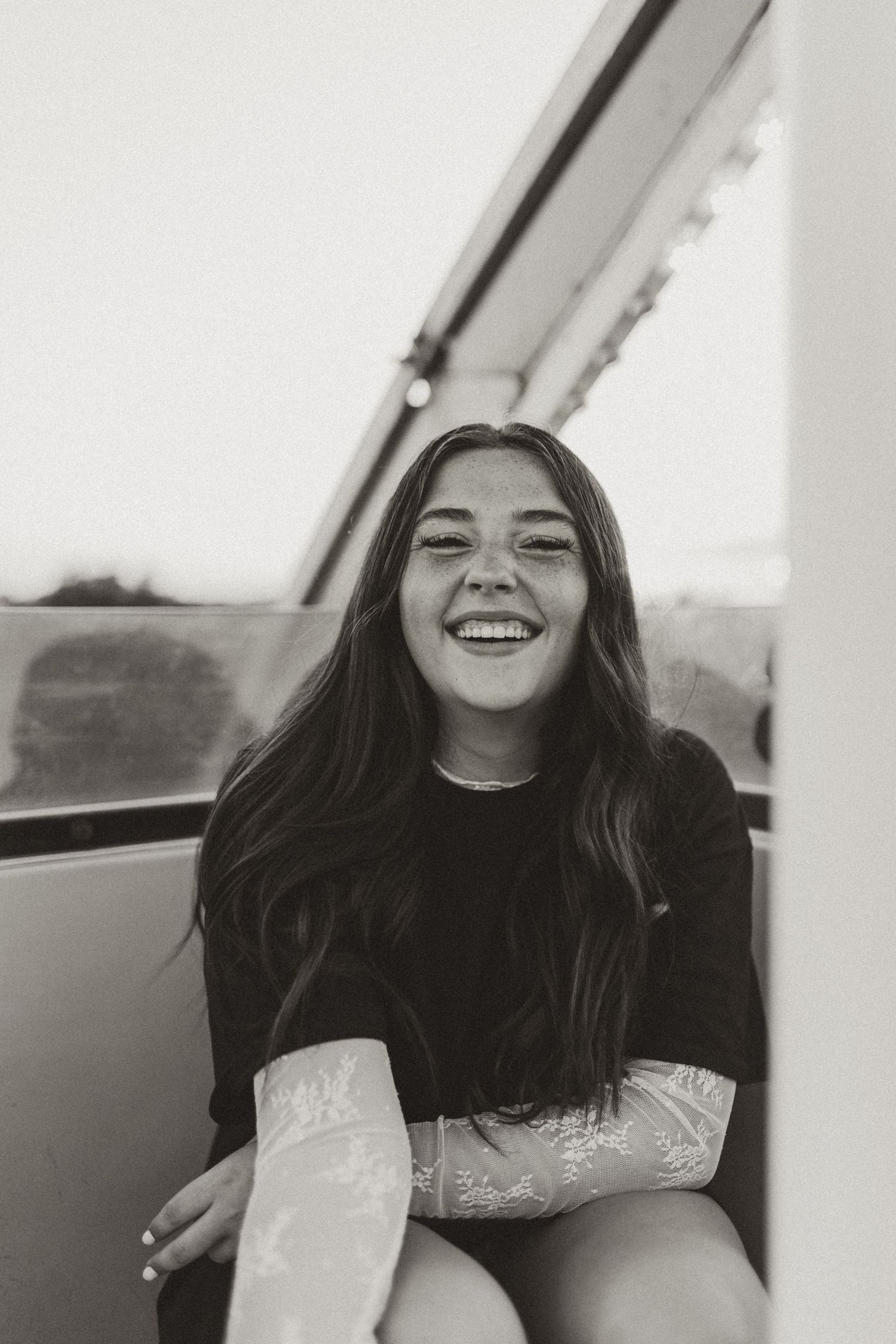 Black and white photo of laughing young woman sitting on a ferris wheel gondola.