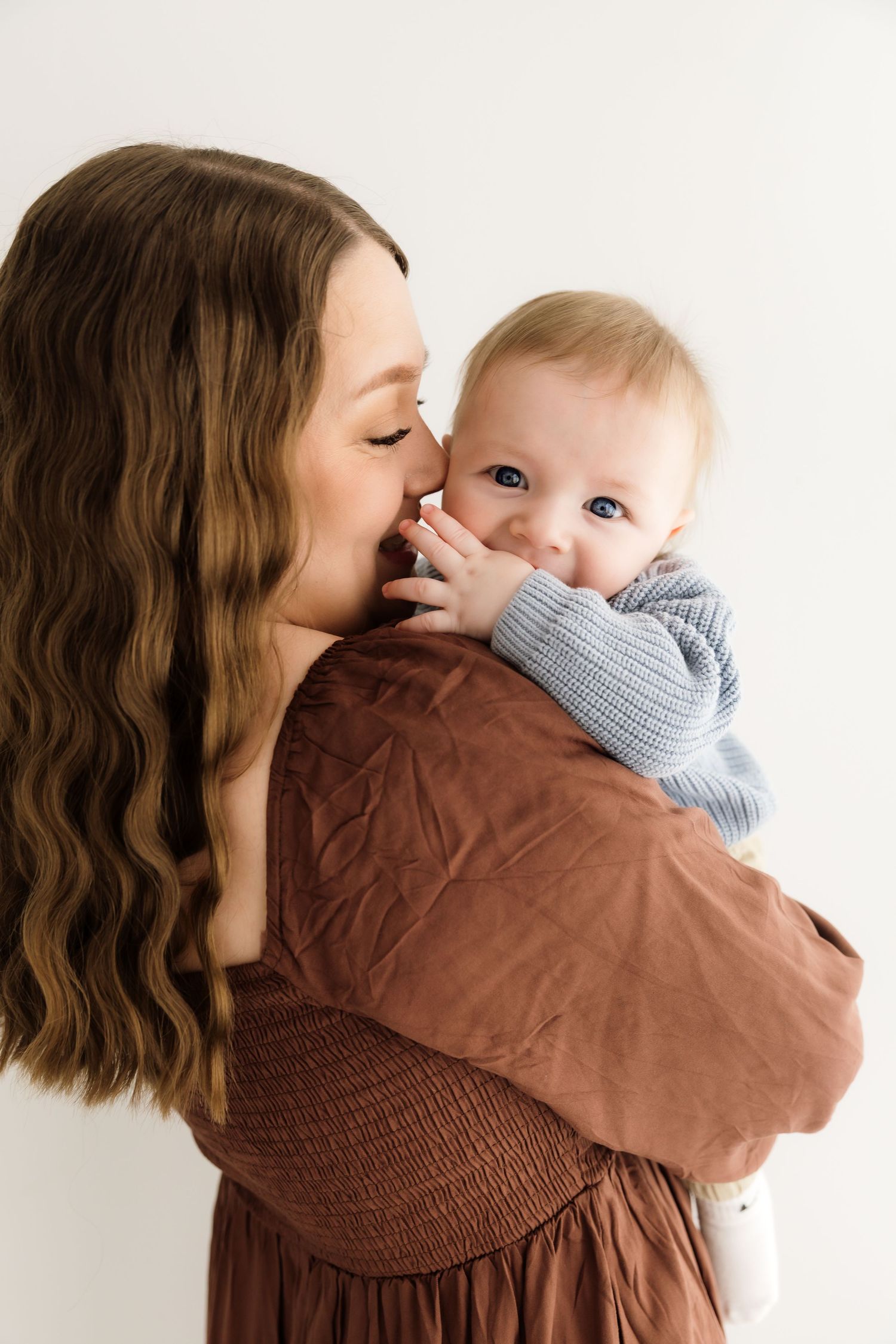 Mother with long wavy hair kissing her blue-eyed baby in a blue sweater.