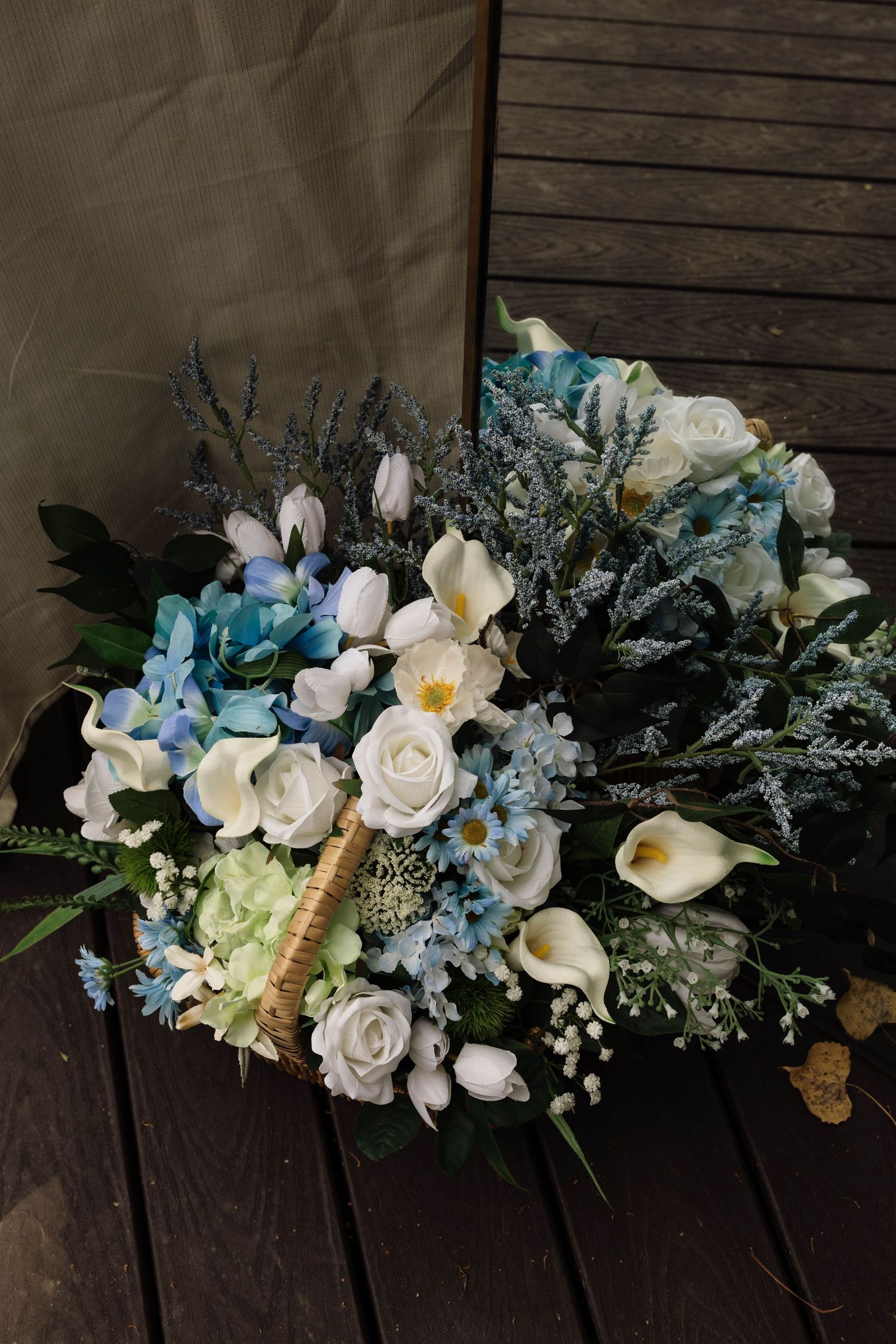 Lush bridal bouquet of white roses, blue hydrangeas, calla lilies, and wildflowers in a wicker basket.
