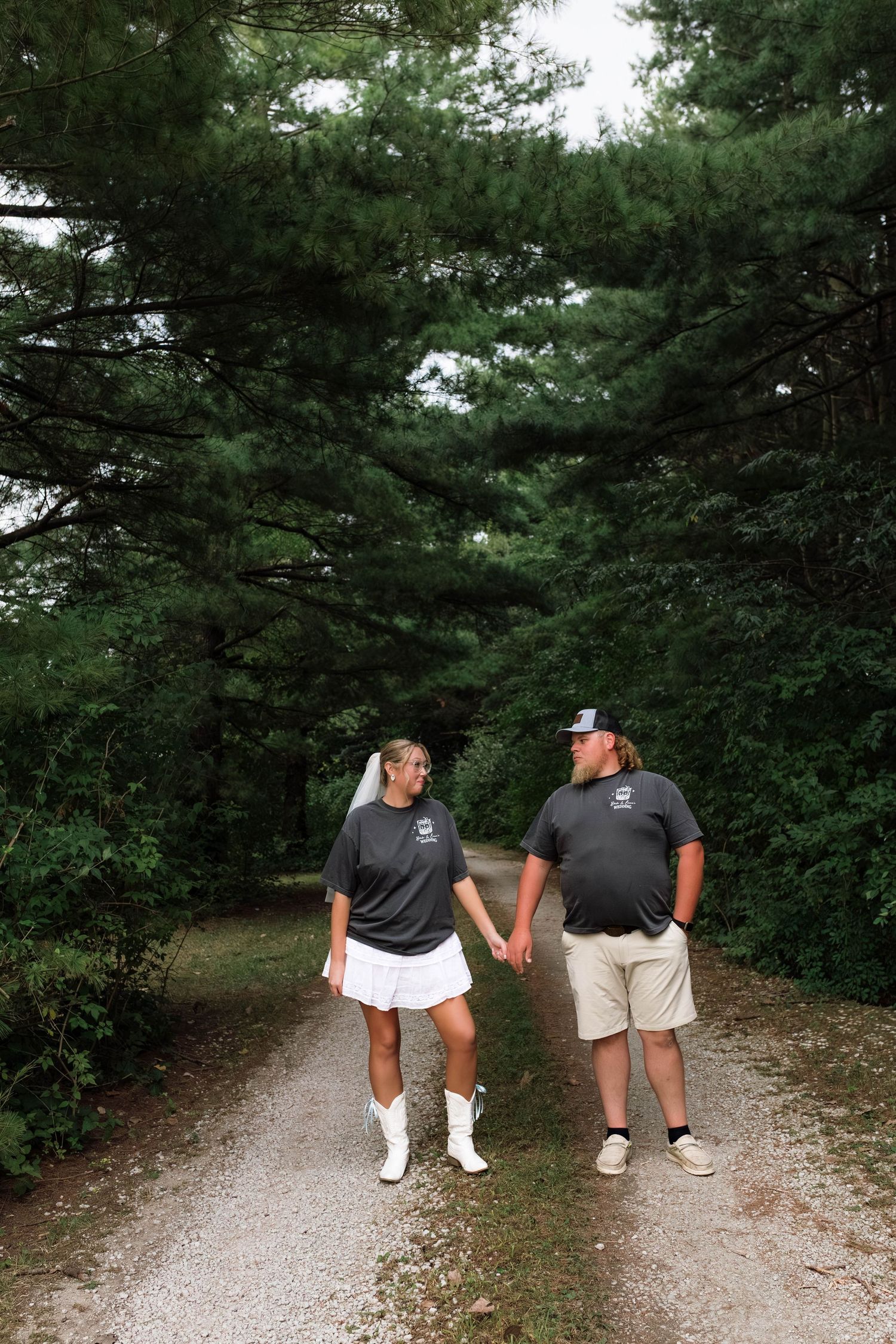 Couple holding hands walking down a tree-lined gravel path, wearing matching dark shirts.