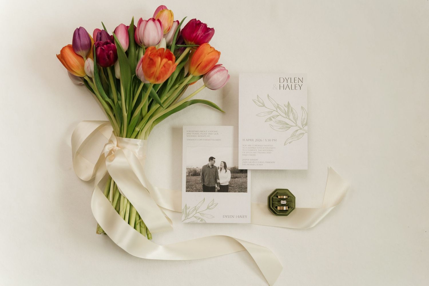Elegant wedding flat lay with colorful tulip bouquet, ribbon, stationery suite, and vintage photo.