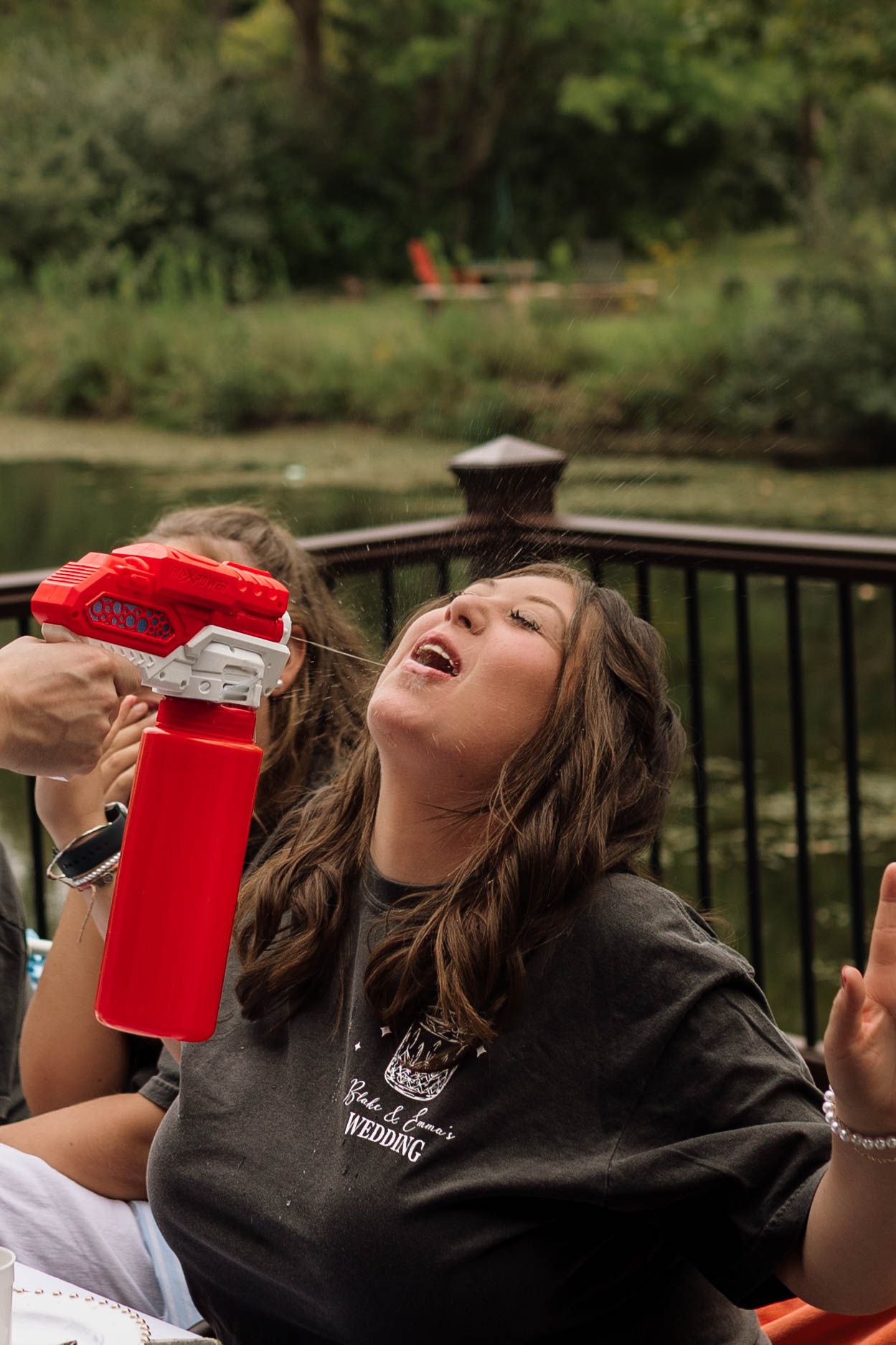 Young woman laughing while drinking from a red water gun on an outdoor deck.