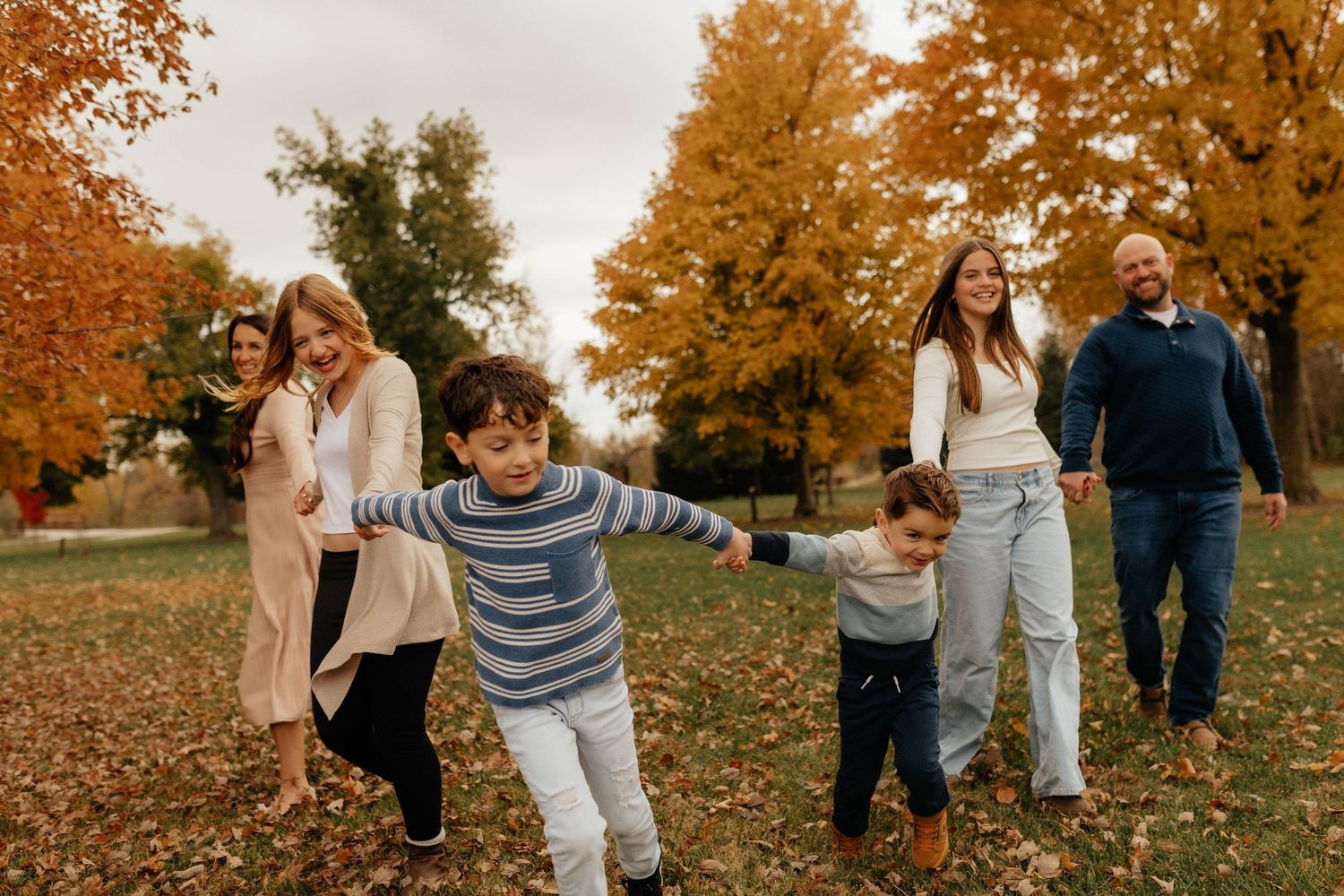 Joyful family walking together in autumn park with children running ahead through colorful fall leaves.