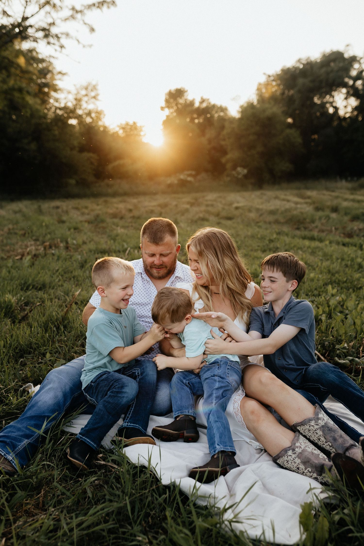 Happy family of five sitting together on a blanket in a golden sunset meadow.