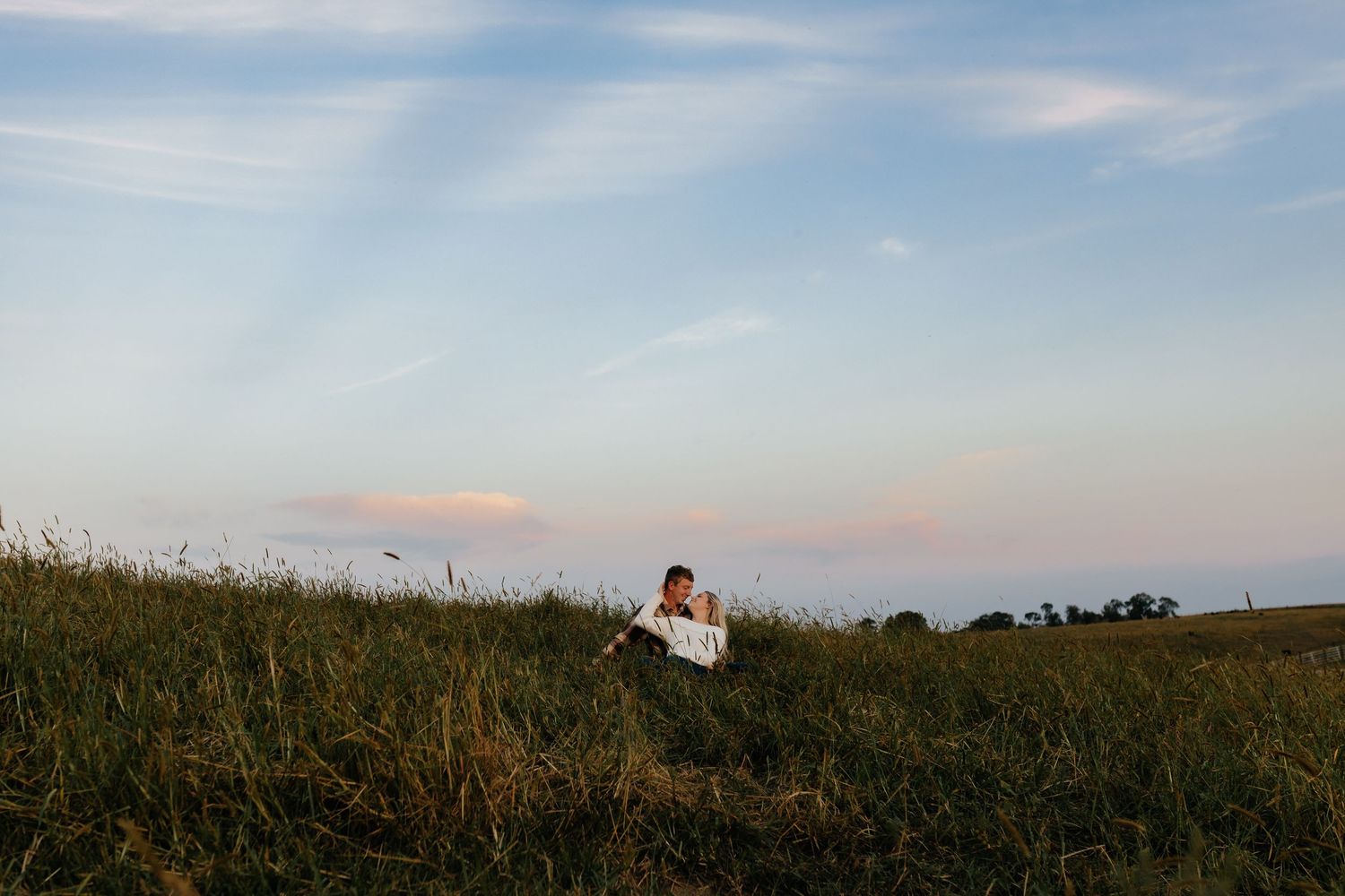 A person relaxes in a green meadow beneath a beautiful blue and pink sky.