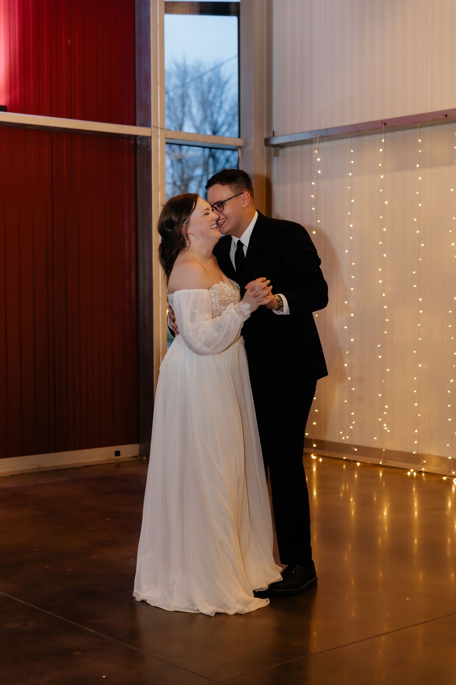 Bride and groom share romantic first dance near twinkling string lights in warmly lit wedding reception venue.