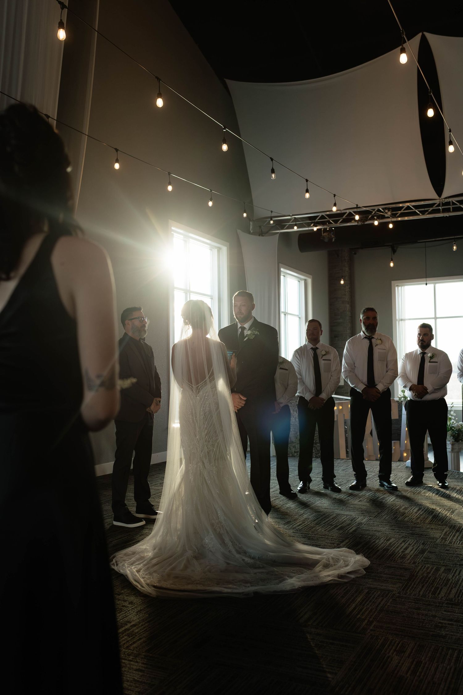 Bride and groom exchange vows at an indoor wedding ceremony with warm string lights glowing.