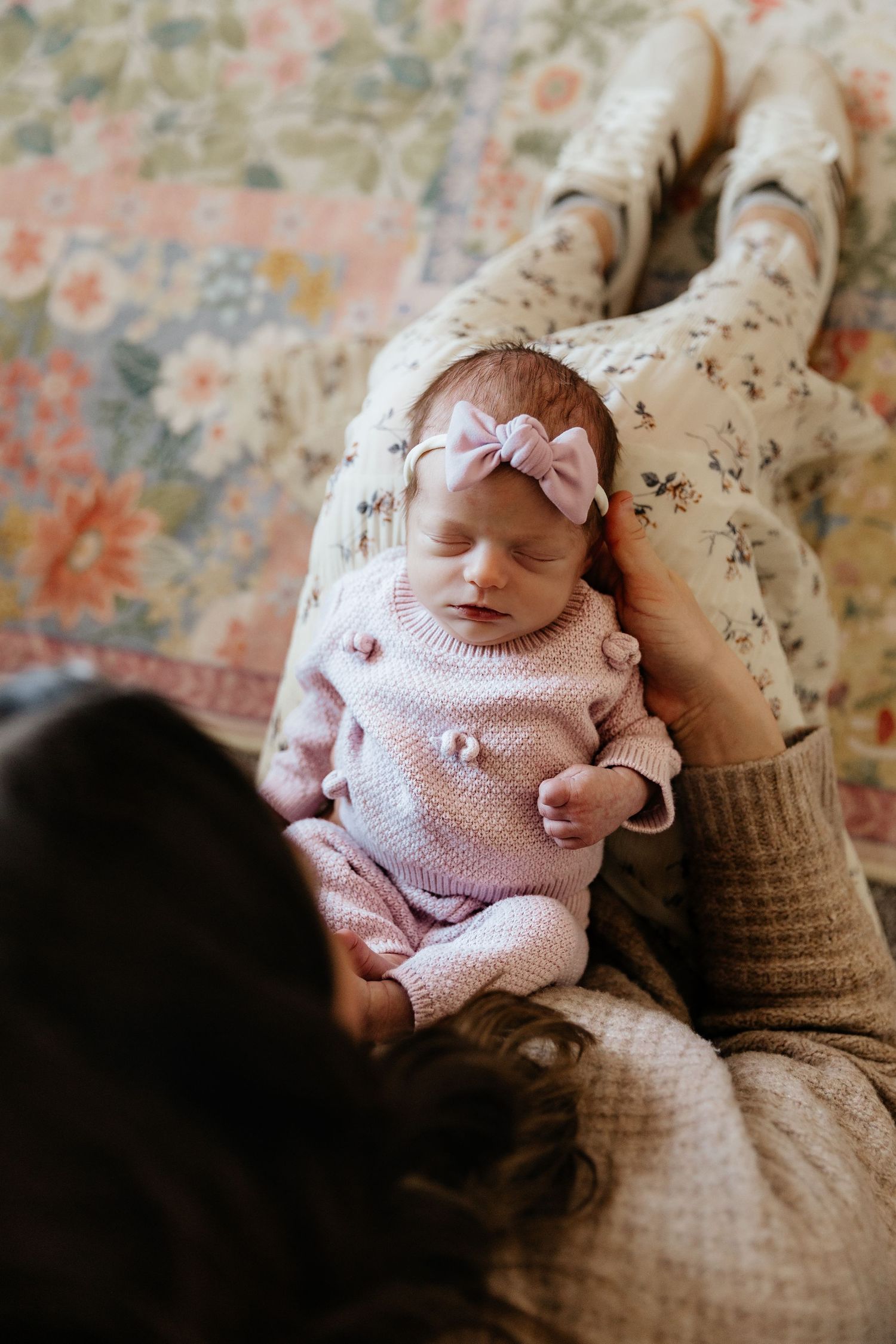 Mother gazes lovingly at newborn baby girl in pink knit outfit with bow headband.
