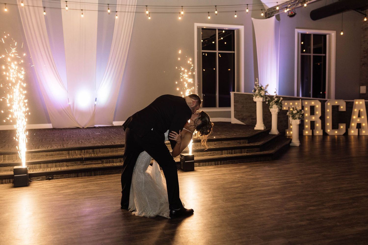 Bride and groom share a romantic dip dance on the dance floor surrounded by sparkling fountains.