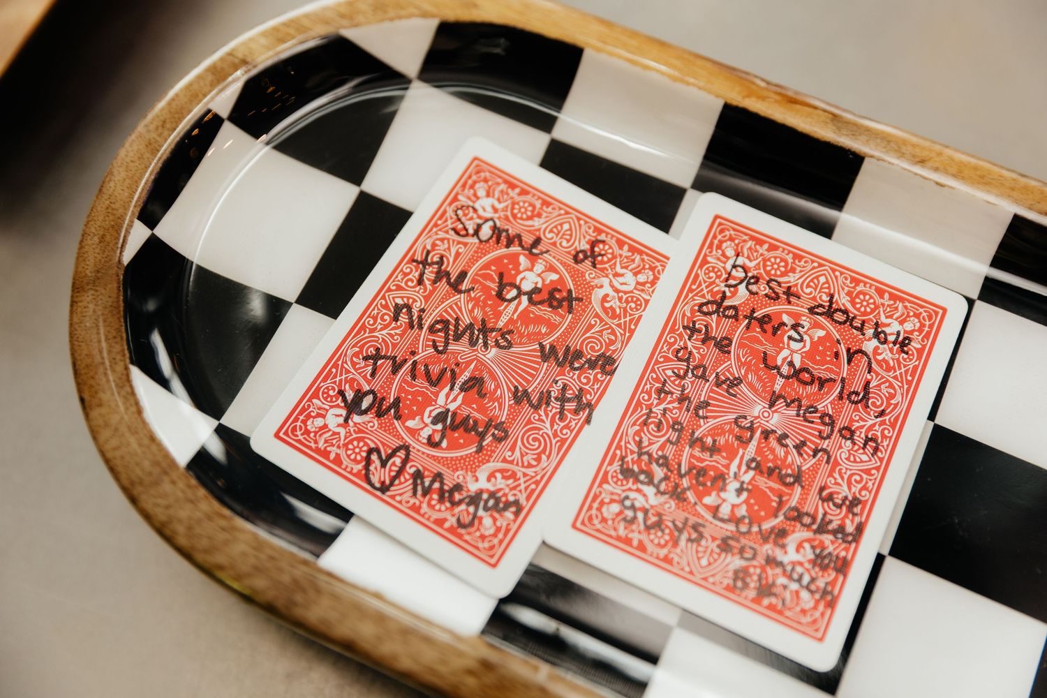 Handwritten love notes on red playing cards displayed in a wooden checkered tray as wedding keepsakes.
