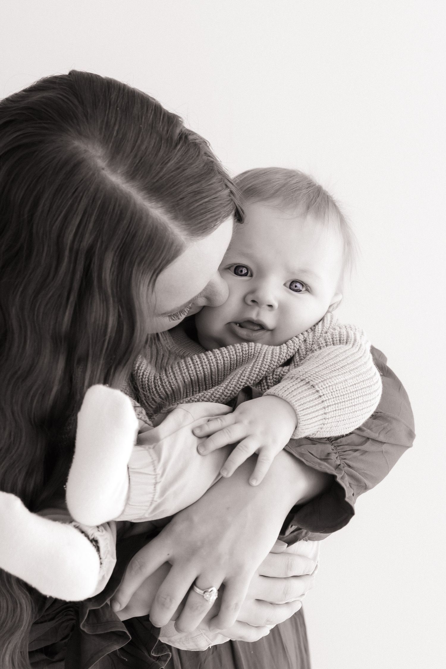 Black and white image of mother kissing her baby while holding a stuffed toy.