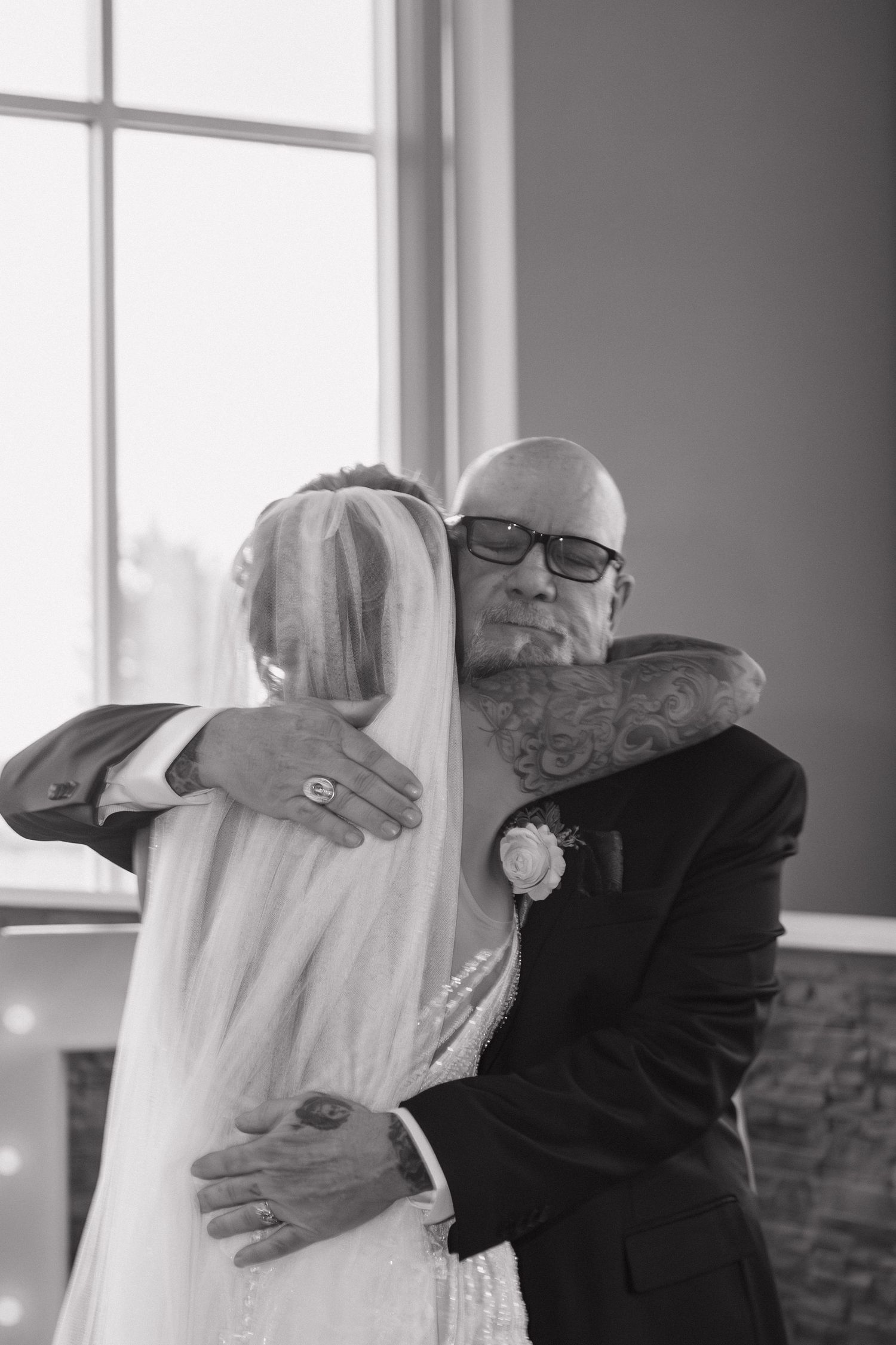 Emotional black and white photo of tattooed father hugging bride in wedding veil.