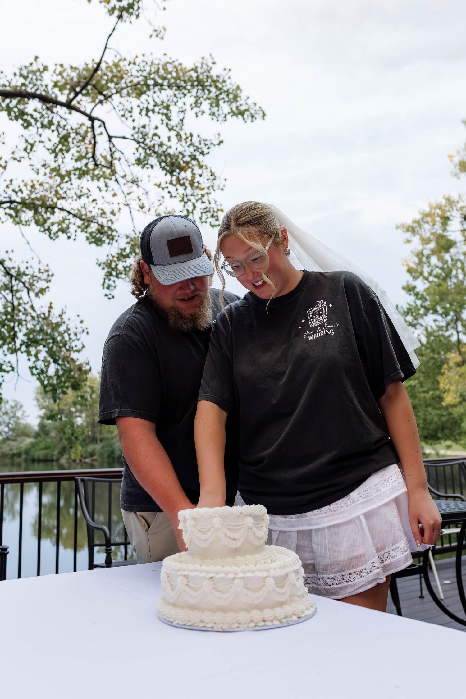 Bride and groom cutting a two-tiered white wedding cake on an outdoor deck.