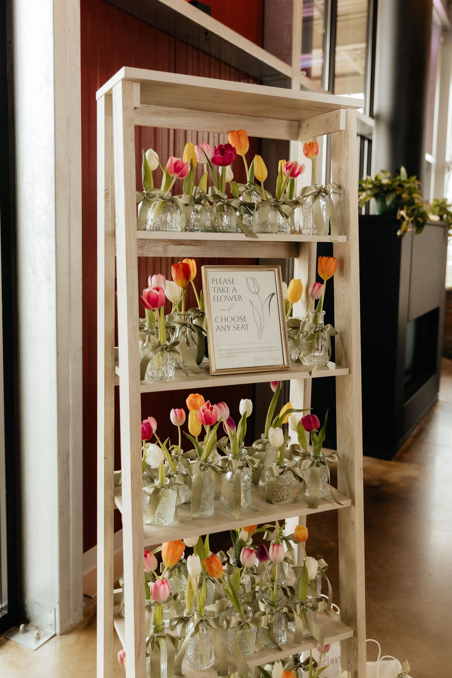 Wooden shelf display with colorful tulips in glass vases and a sign reading please take a flower at a wedding.