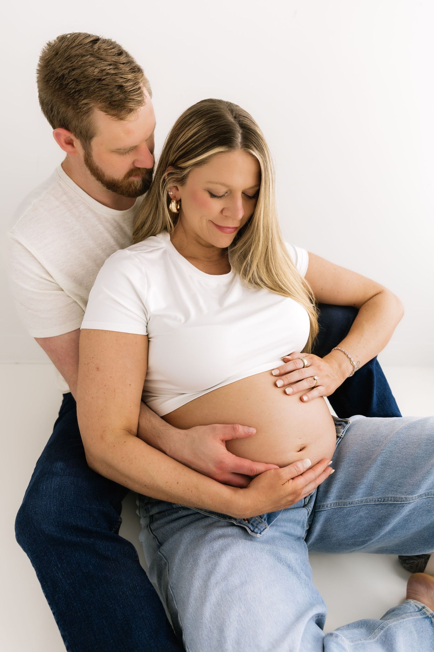 Couple sharing tender moment, man embracing pregnant woman from behind as they both cradle her baby bump.