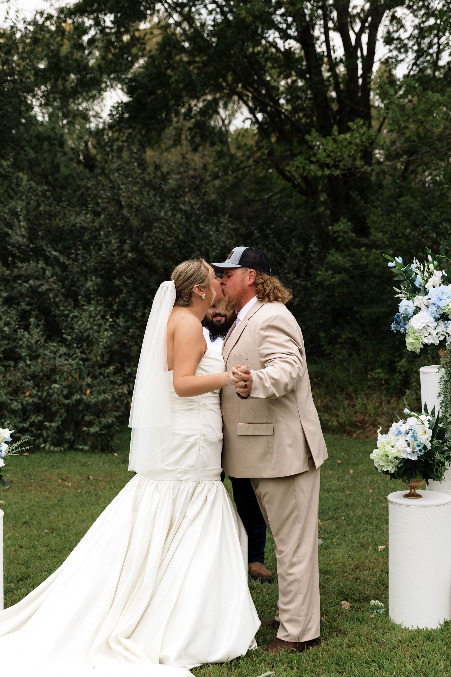 Bride and groom share first kiss at outdoor wedding altar with blue floral arrangements.