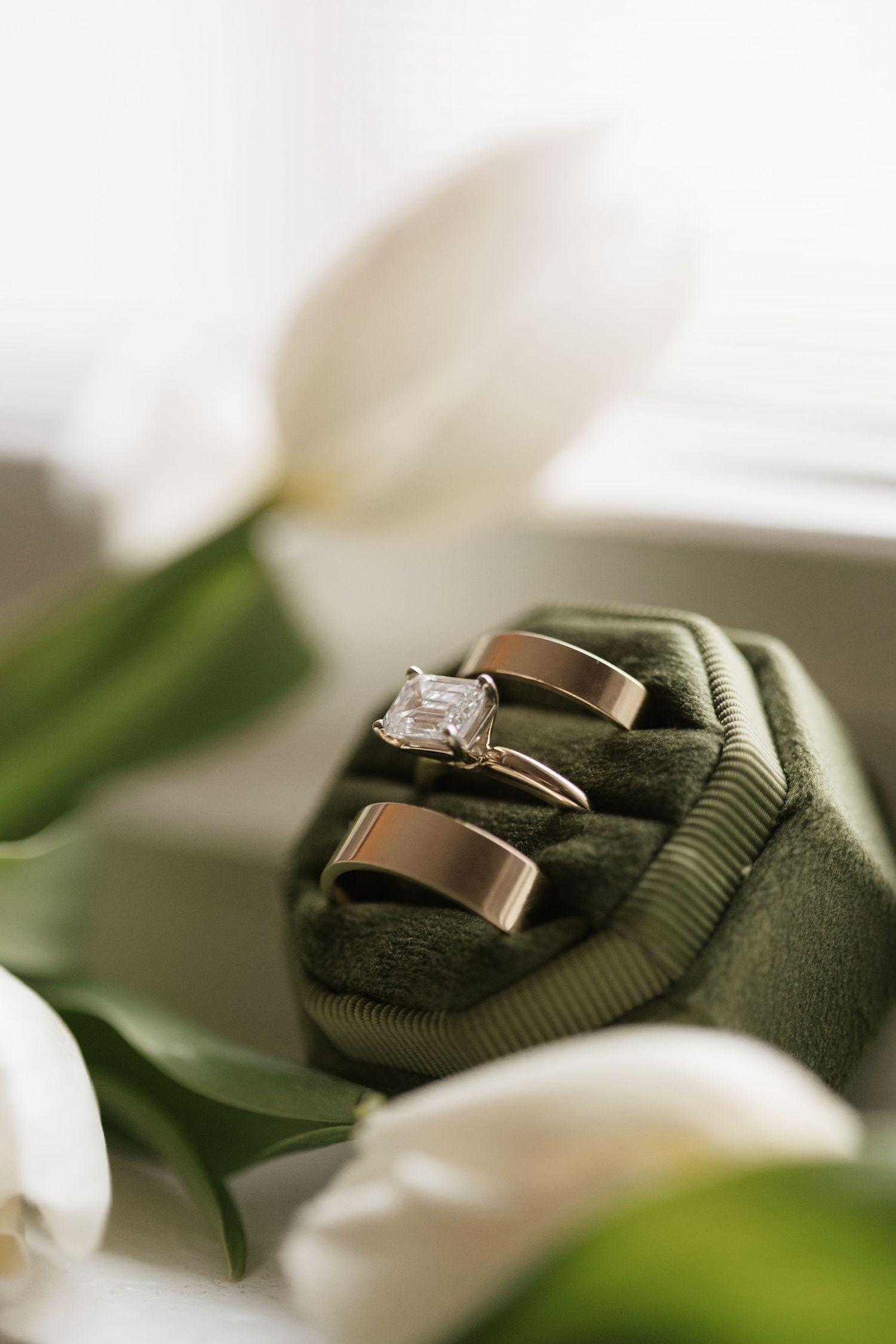 Three rose gold wedding rings including diamond engagement ring in green velvet box with white tulips.