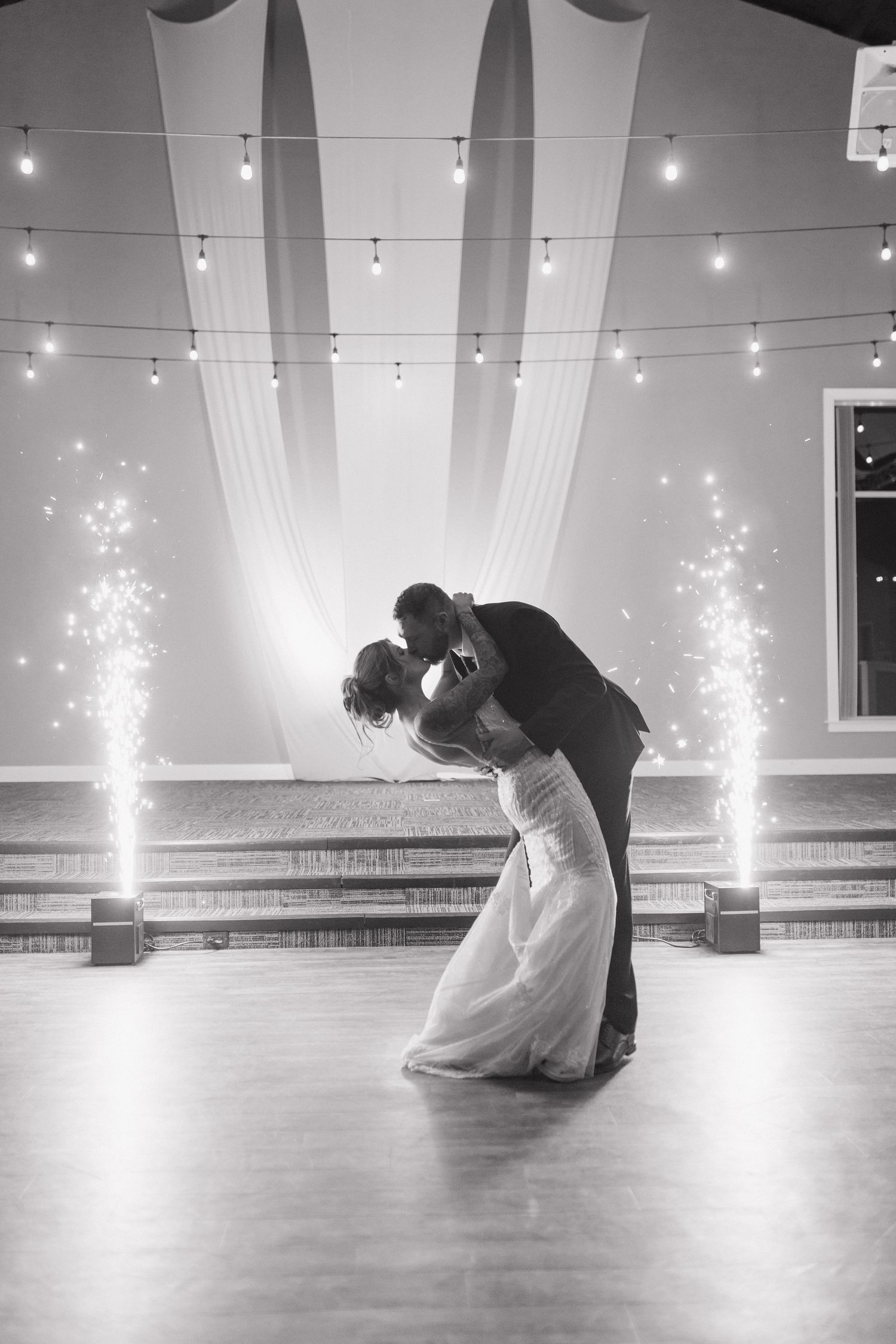 Bride and groom share romantic dip kiss with sparkling fountains on elegant wedding dance floor.