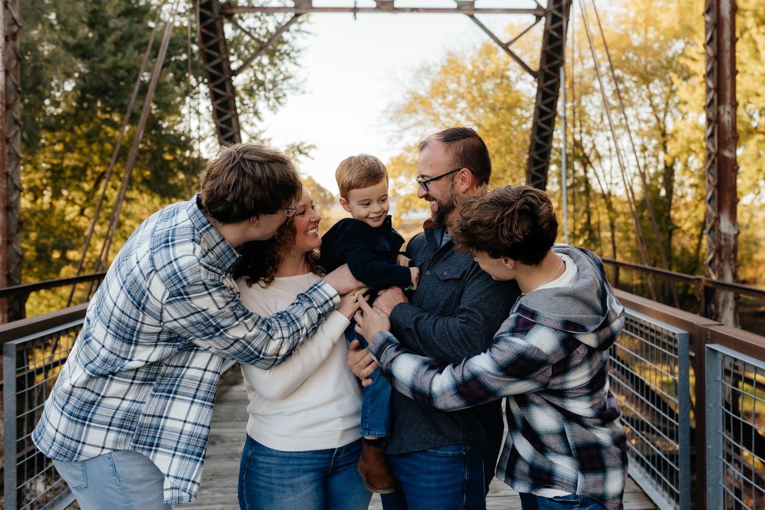 Joyful family of five gathers on bridge surrounded by colorful autumn foliage.