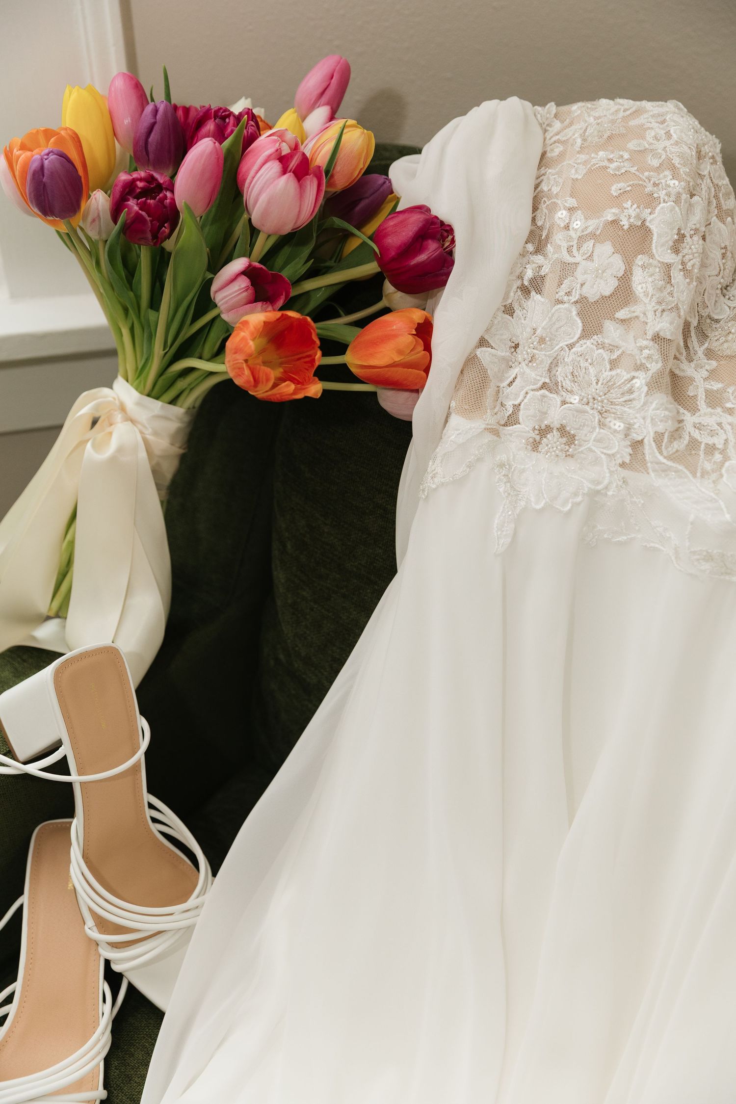 White lace wedding gown displayed with colorful tulip bouquet and strappy white heeled sandals.