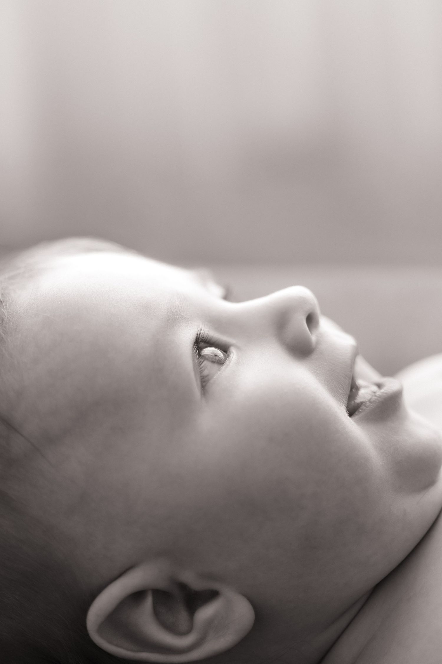 Black and white close-up profile of a smiling baby looking upward.