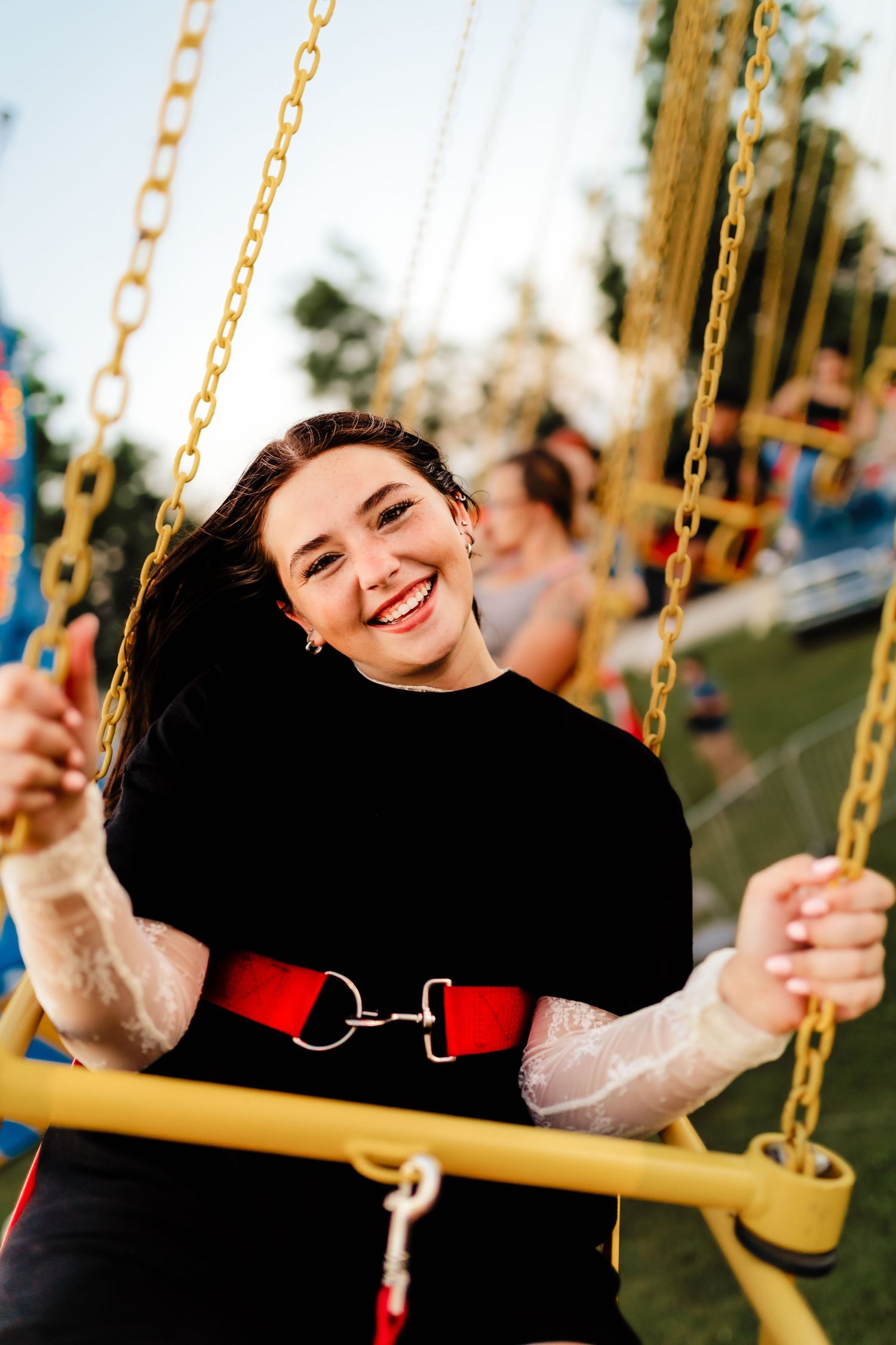 Happy young woman riding a chain swing carousel ride at an amusement park on a sunny day.