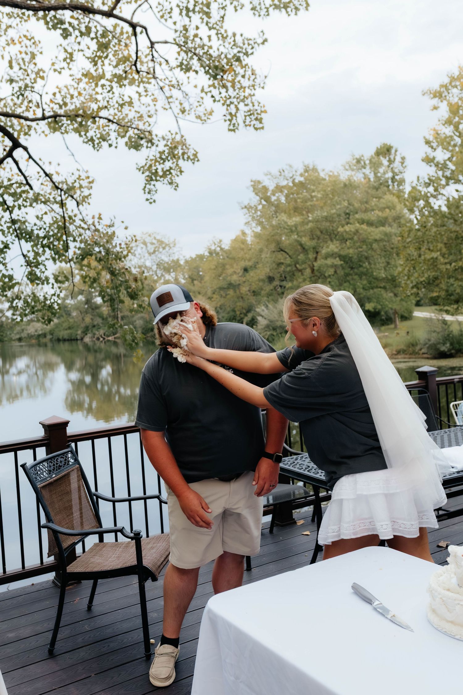 Bride playfully smashing wedding cake into grooms face on an outdoor deck.