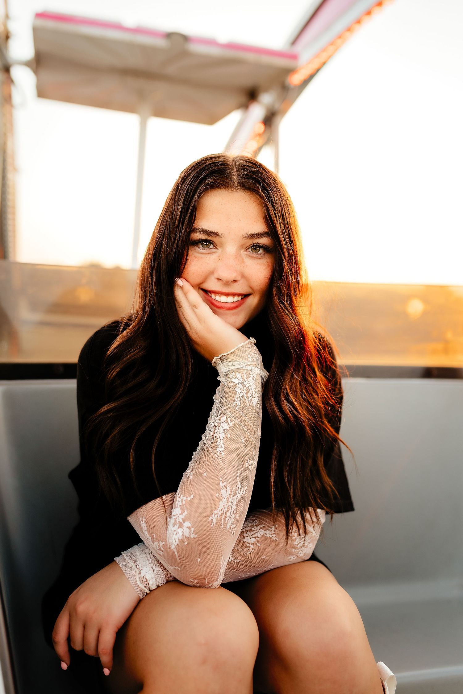 Young woman with long dark hair smiling at sunset while sitting on a carnival ride gondola.