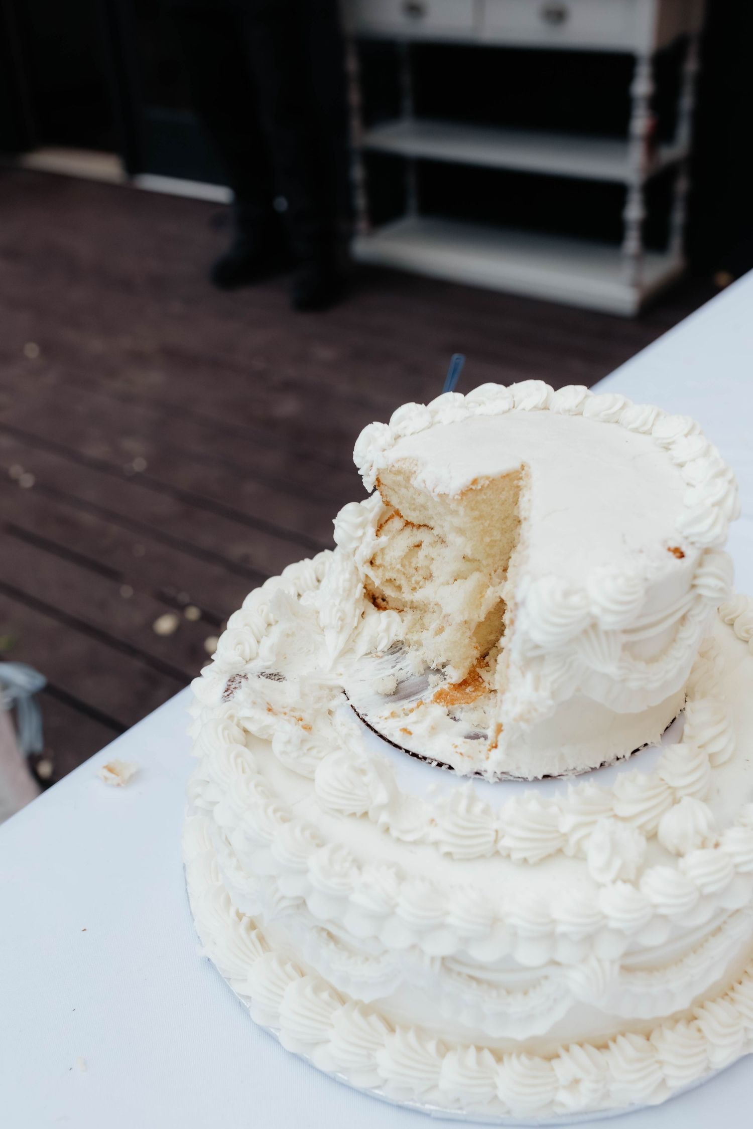Two-tiered white wedding cake with a slice removed on a white tablecloth.