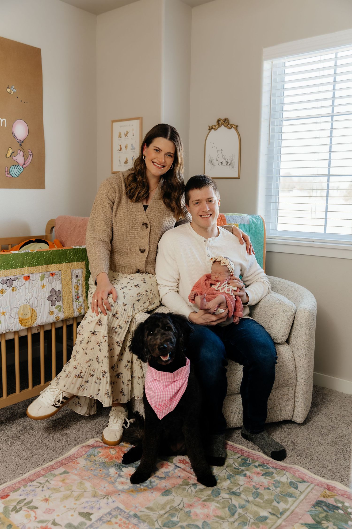Happy family with mom, dad, newborn baby, and black dog pose in baby nursery.