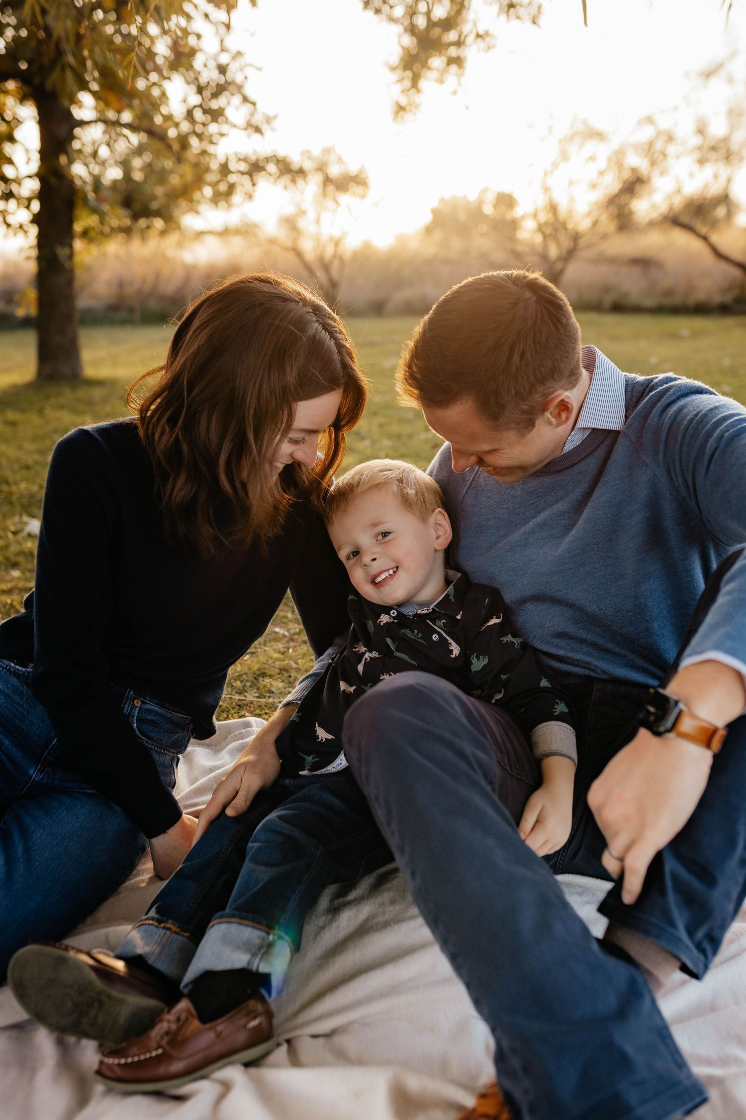 Happy family of three sitting on a blanket in a sunlit autumn park at golden hour.