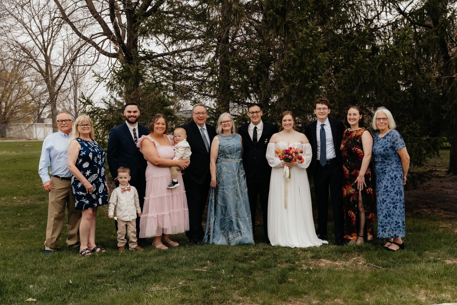 Large extended family gathers for group wedding portrait on green lawn outdoors.