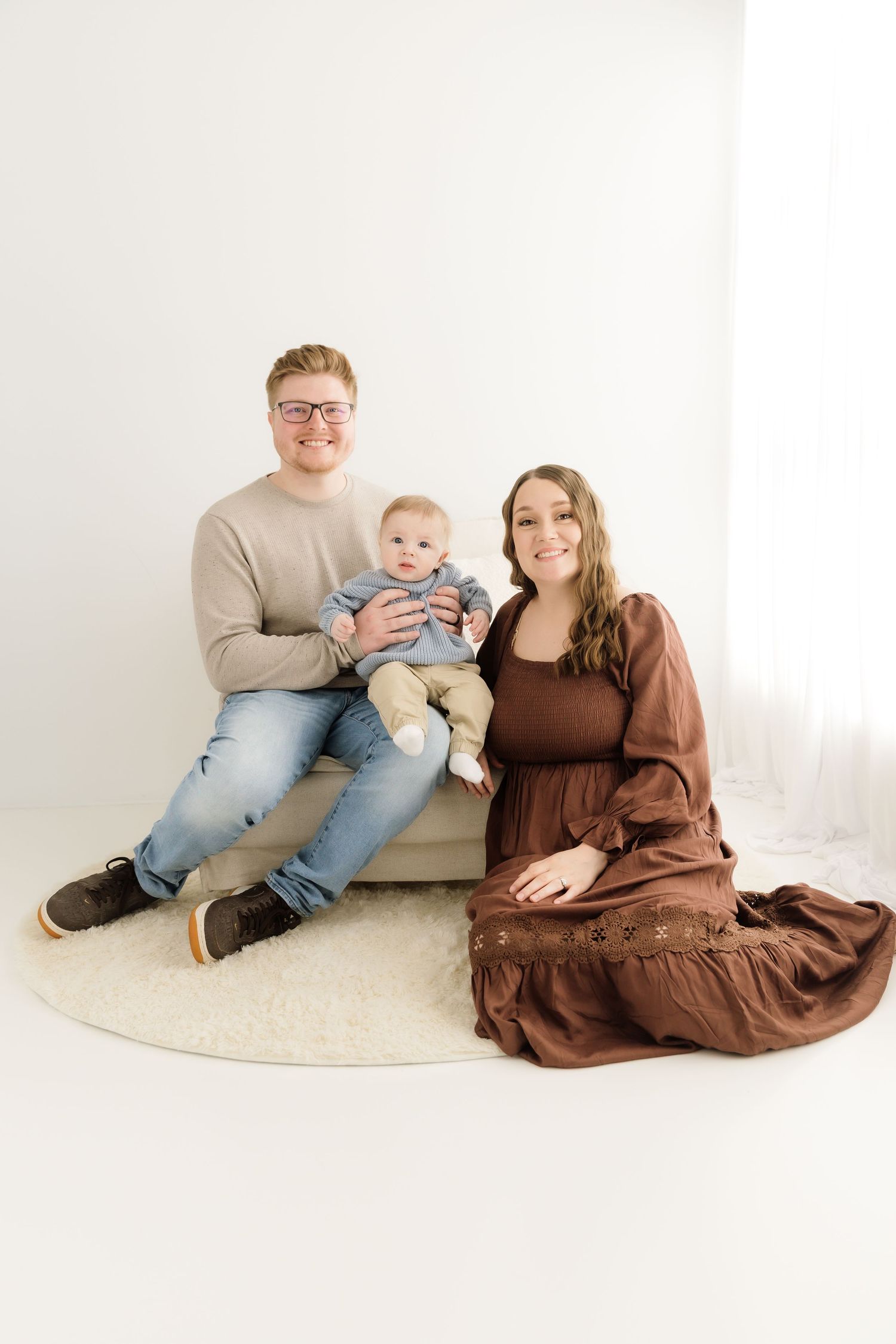 Happy family portrait with father holding baby and mother in brown dress seated.