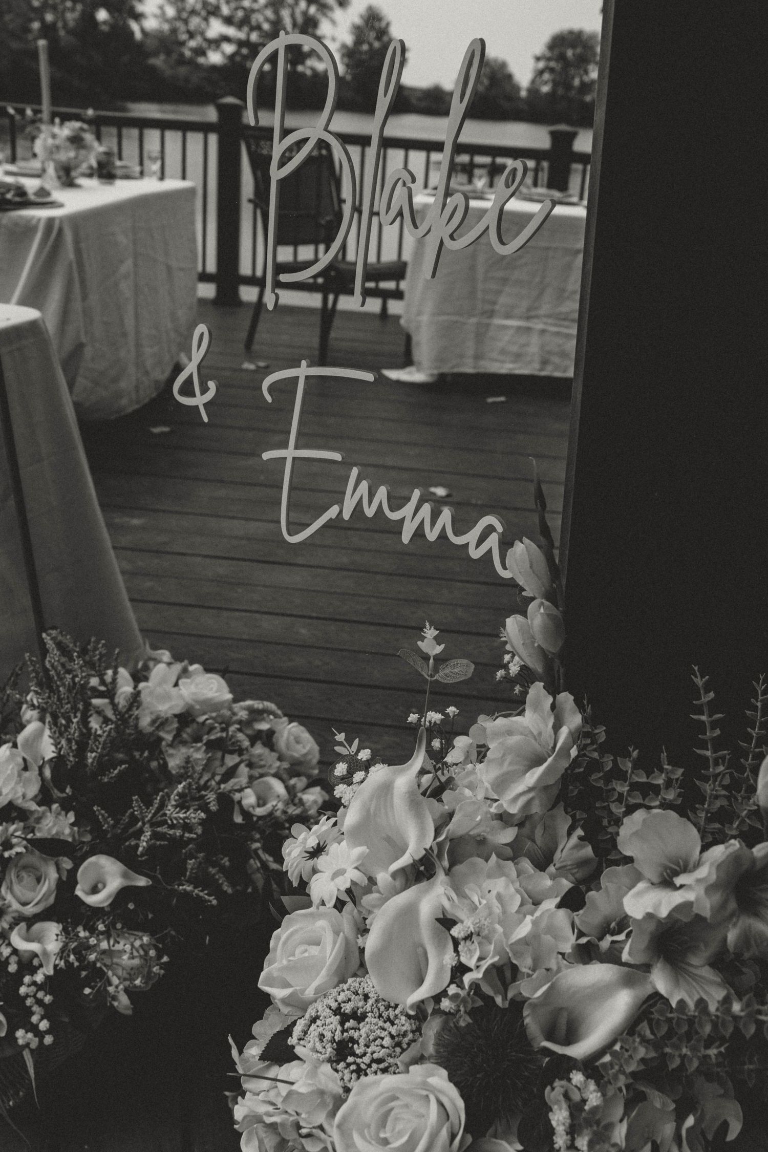 Black and white wedding sign reading Blake and Emma surrounded by white roses and calla lilies.