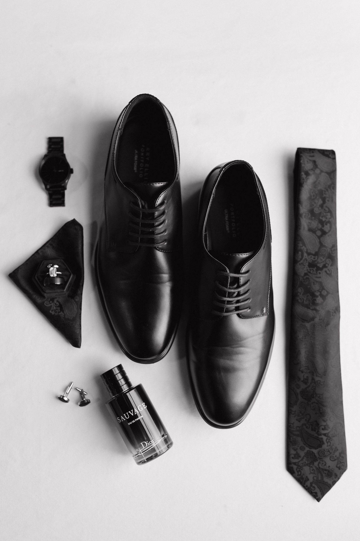 Black and white groom flat lay with dress shoes, Dior cologne, tie, watch, and cufflinks.