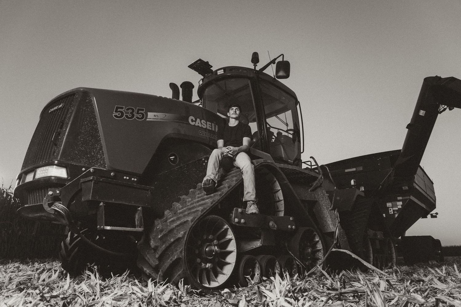 Black and white photo of person sitting on large Case IH tracked tractor in a field.