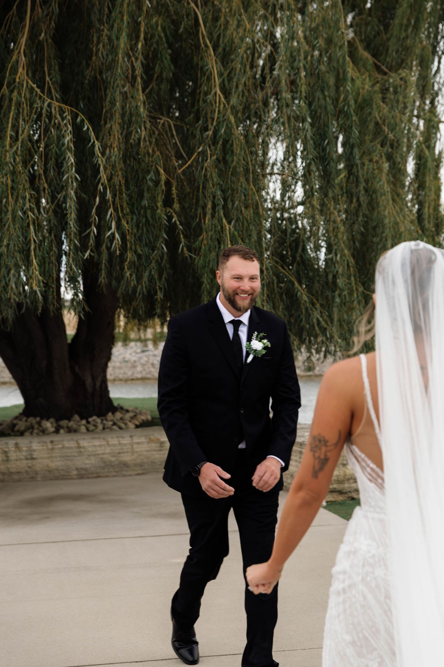 Smiling groom in black suit reacts with joy seeing his bride for the first time at their wedding.