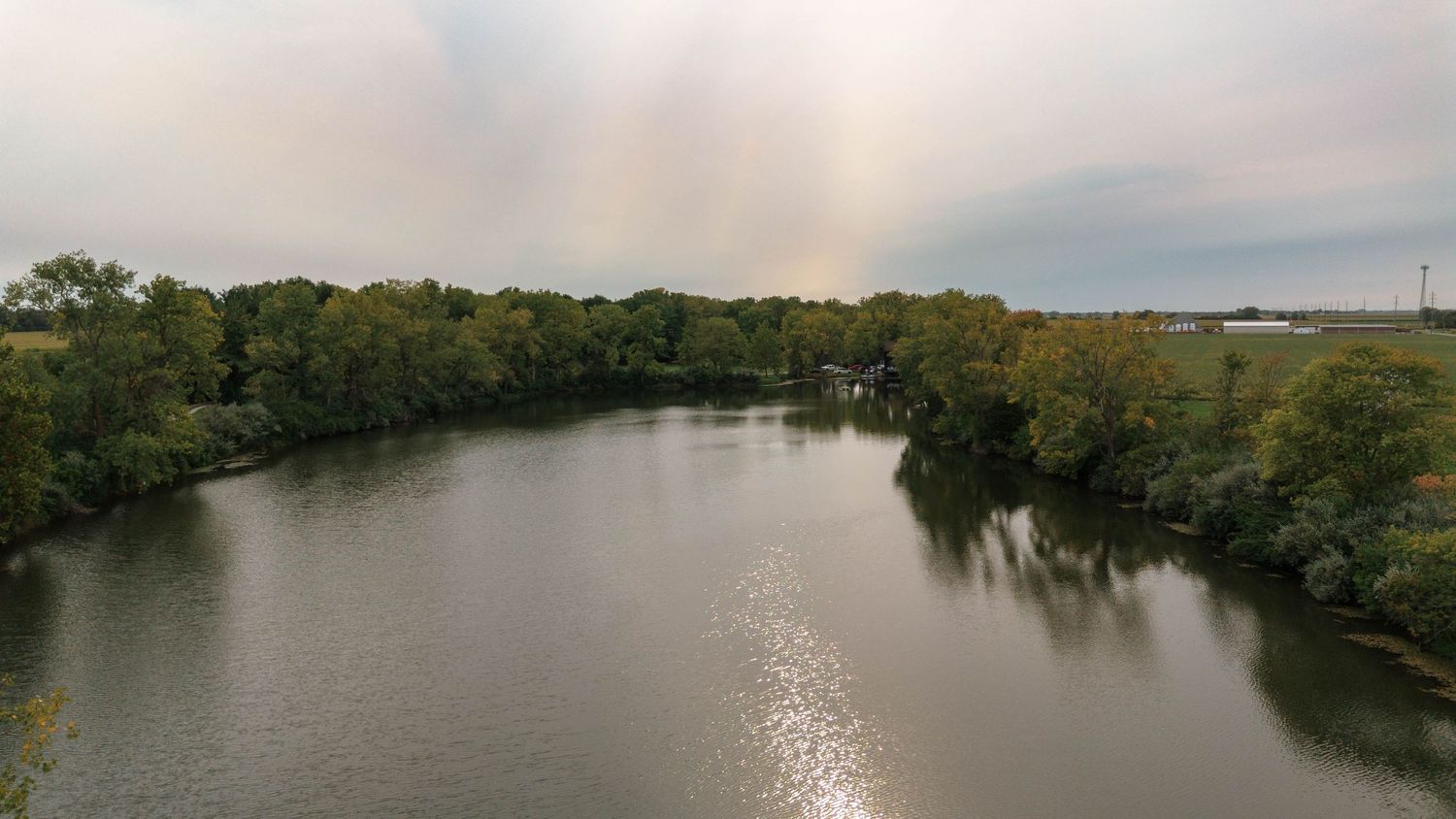 Aerial drone view of a winding river bordered by dense green trees under a cloudy sky.