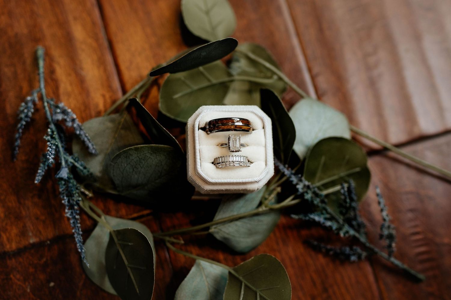His and hers wedding rings displayed in white velvet box surrounded by eucalyptus and lavender sprigs.