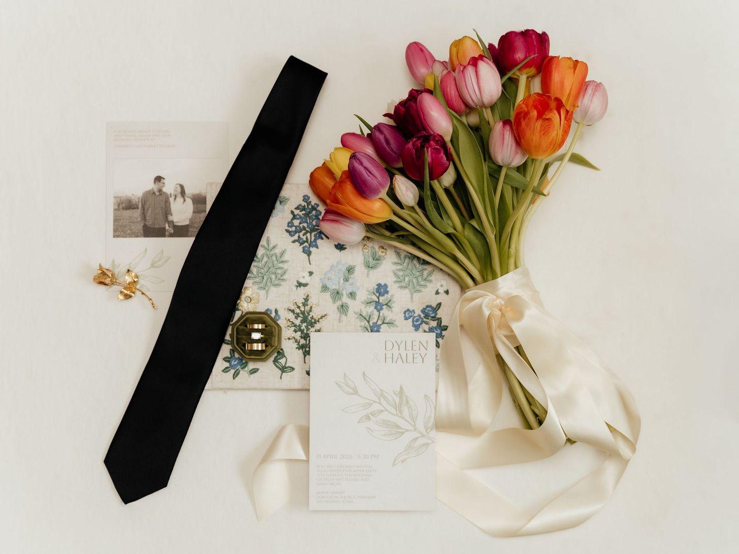 Flat lay of colorful tulip bouquet, black tie, wedding stationery, and vintage photo.