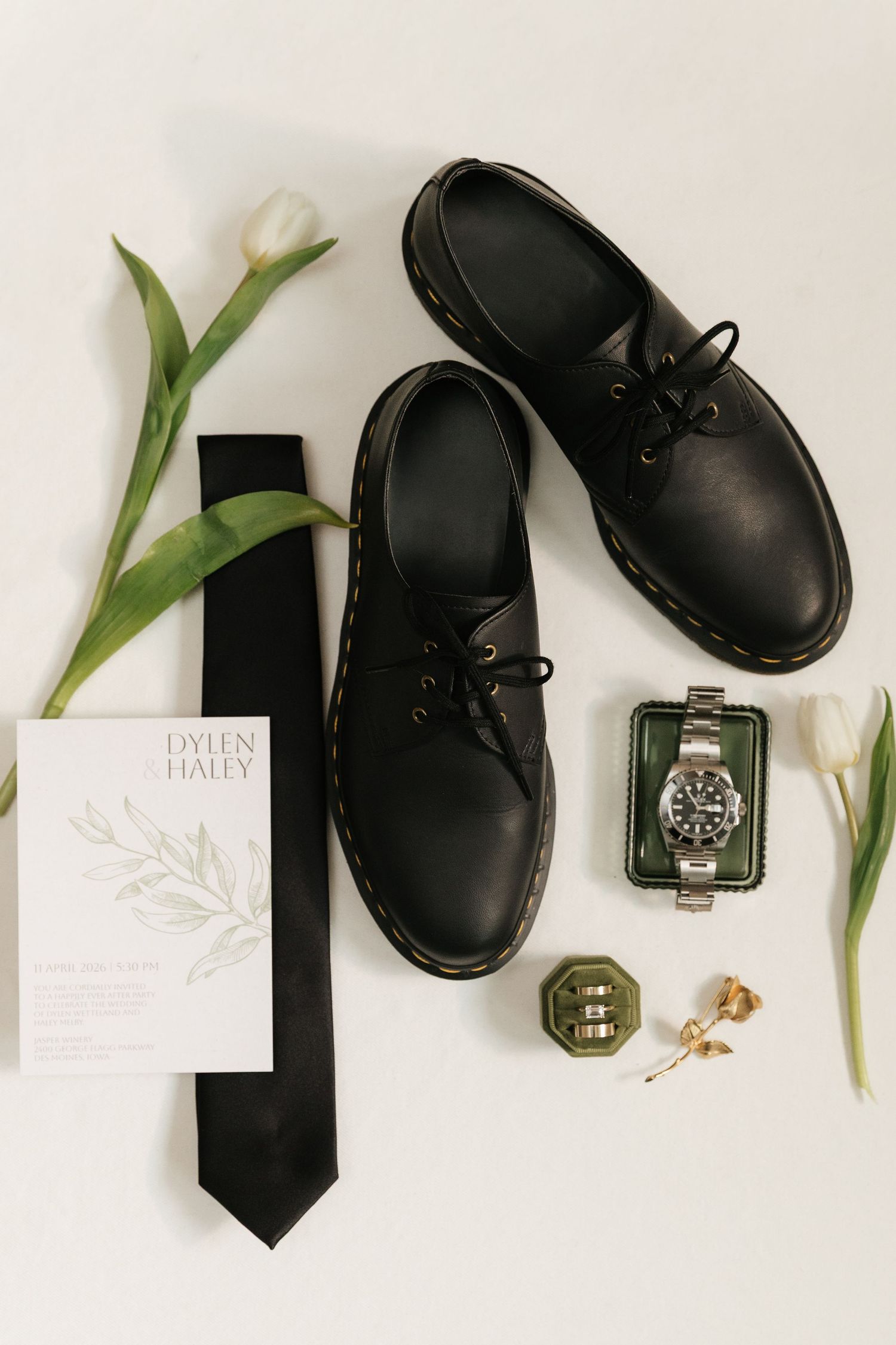 Groom flat lay with black Dr. Martens shoes, tie, Rolex watch, ring box, and wedding invitation.