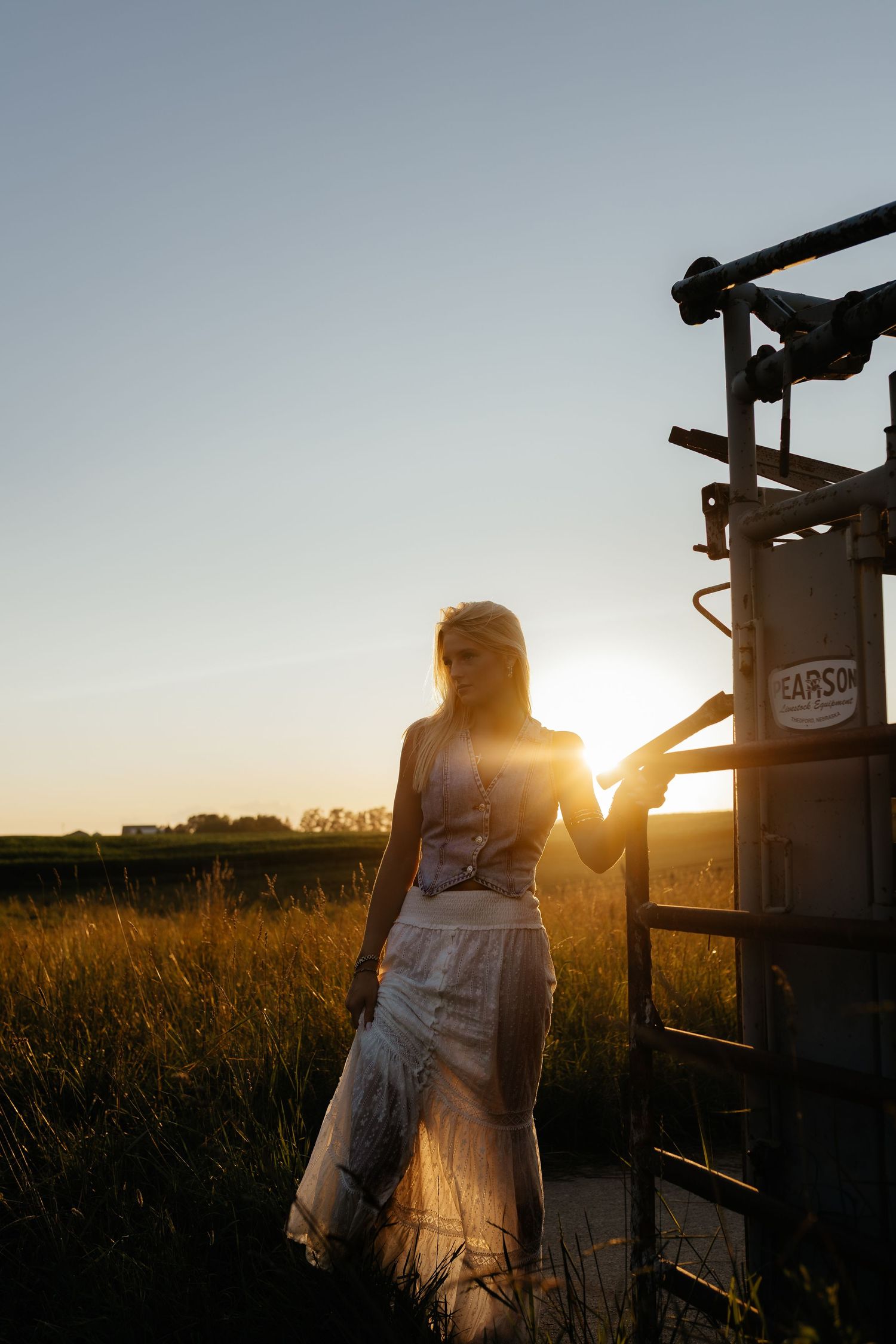 Blonde woman silhouetted against golden sunset in field beside farm equipment.